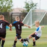Kids football – Three children playing soccer on a grass field with a goal in background